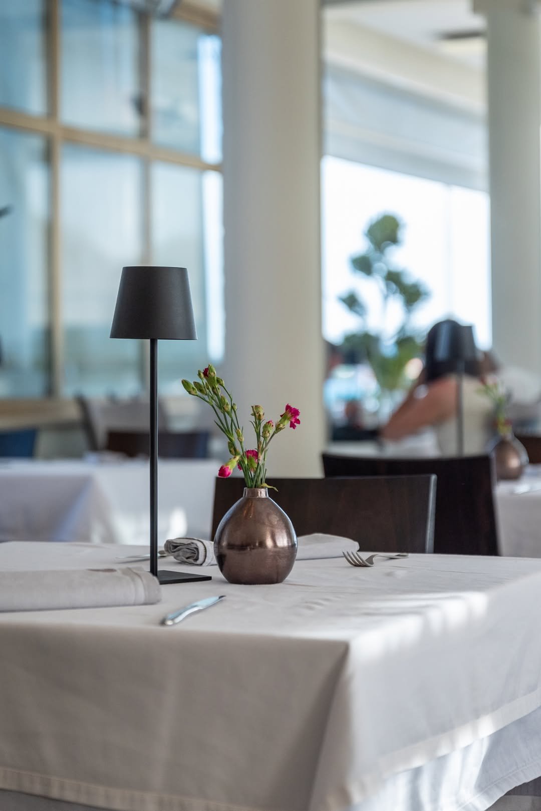 Minimalistički interijer restorana — crna stolna lampa, mali vrč, bijelo platno