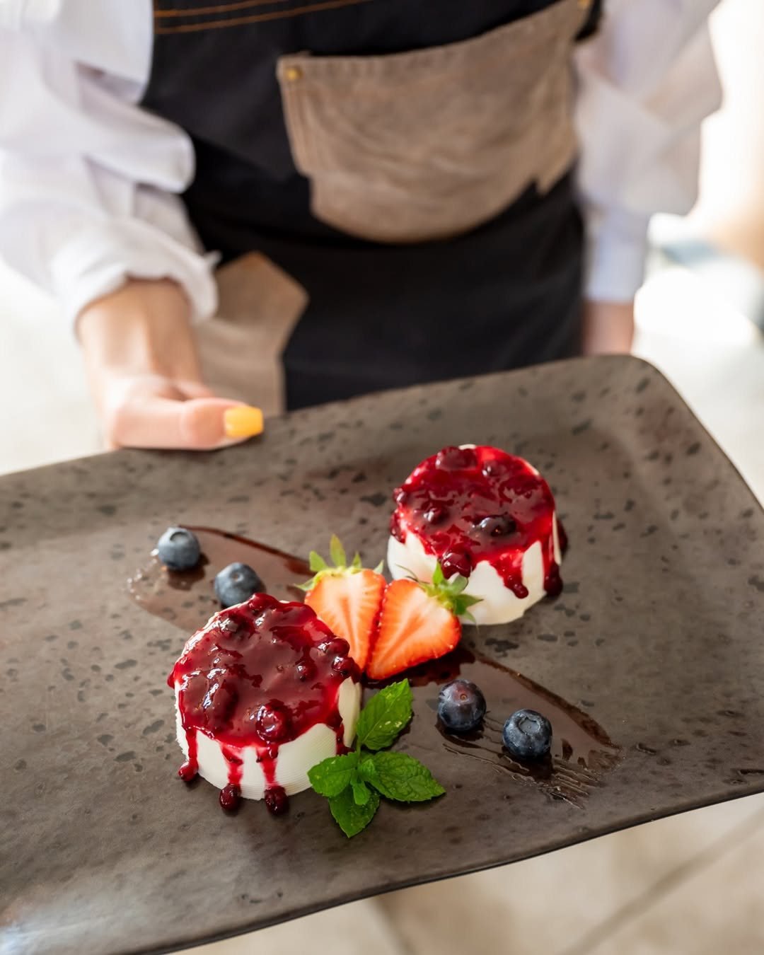 Panna cotta s preljevom od bobičastog voća, jagodama i borovnicama na tamnoj keramici